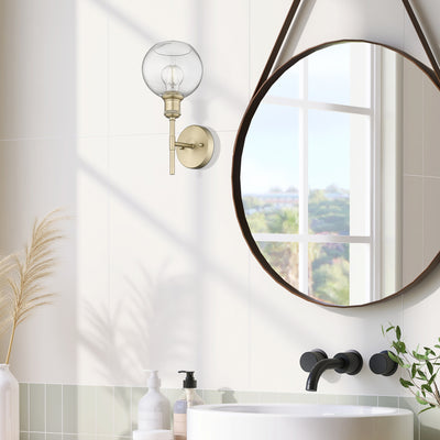Axel 1-light Wall Sconce in Brushed Champagne Brass and Globe Clear Glass, shown in a room setting - Golden Lighting