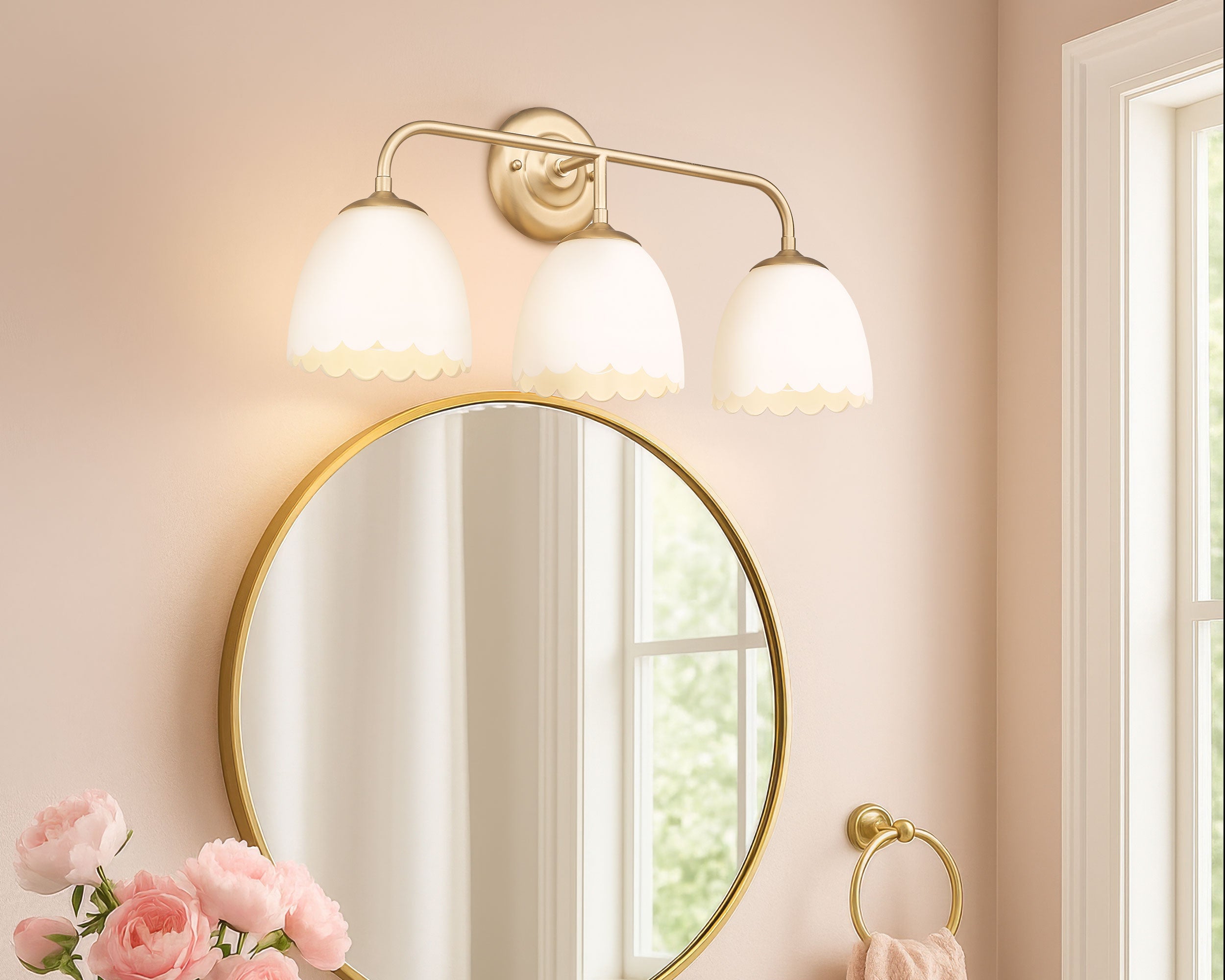 Bathroom with round mirror, gold light fixture, and pink flowers on a counter.