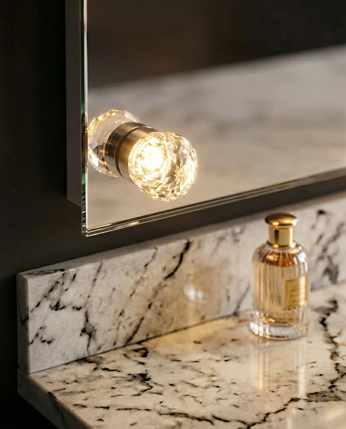 Wall-mounted Starlight 24" LED Vanity Mirror with a decorative cut crystal diffuser option in a bathroom with marble countertops and backsplash with a perfume bottle in the background.